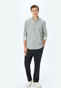 Camisa de botón a rayas en gris y blanco, con mangas largas remangadas, combinada con pantalones oscuros y zapatillas blancas. Textura de tela suave.