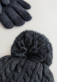 Dunkelblauer Zopfmuster-Mütze mit einem flauschigen Pompon oben, kombiniert mit dunkelblauen Strickhandschuhen mit strukturierten Fingern.