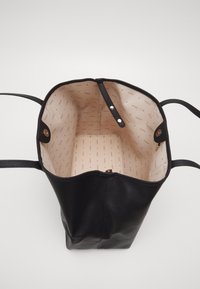 Sac fourre-tout en cuir noir avec une texture douce, une ouverture sur le dessus et un intérieur clair présentant un motif de logo répétitif et deux fermetures à pression.