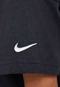 Camiseta de algodón negra con un logotipo bordado de Nike en blanco en la manga izquierda, textura suave y detalle de costura estándar.