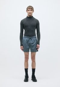 Maglietta nera a maniche lunghe aderente, pantaloni sportivi blu con coulisse, calzini neri e scarpe da ginnastica nere; design pulito e minimale su sfondo semplice.