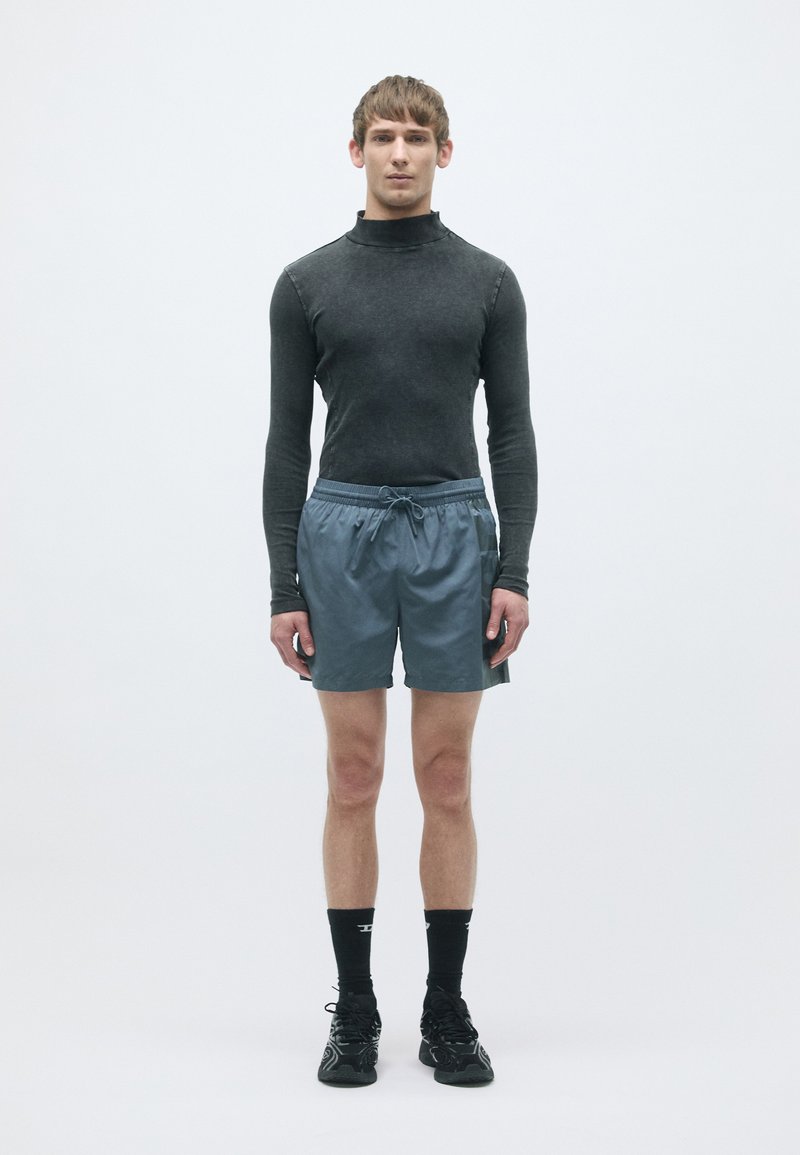 Maglietta nera a maniche lunghe aderente, pantaloni sportivi blu con coulisse, calzini neri e scarpe da ginnastica nere; design pulito e minimale su sfondo semplice.