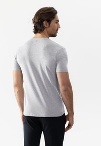 Grijze t-shirt met korte mouwen, gemaakt van zachte stof, met een ronde halslijn en een label op de achterkant van de hals; gecombineerd met donkere broek.