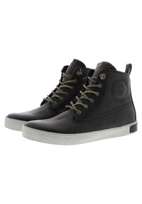 Zapatos de cuero negro de caña alta con ojales plateados, cordones verde oliva y suela de goma blanca. Punta redonda y detalle del logo en el lateral.