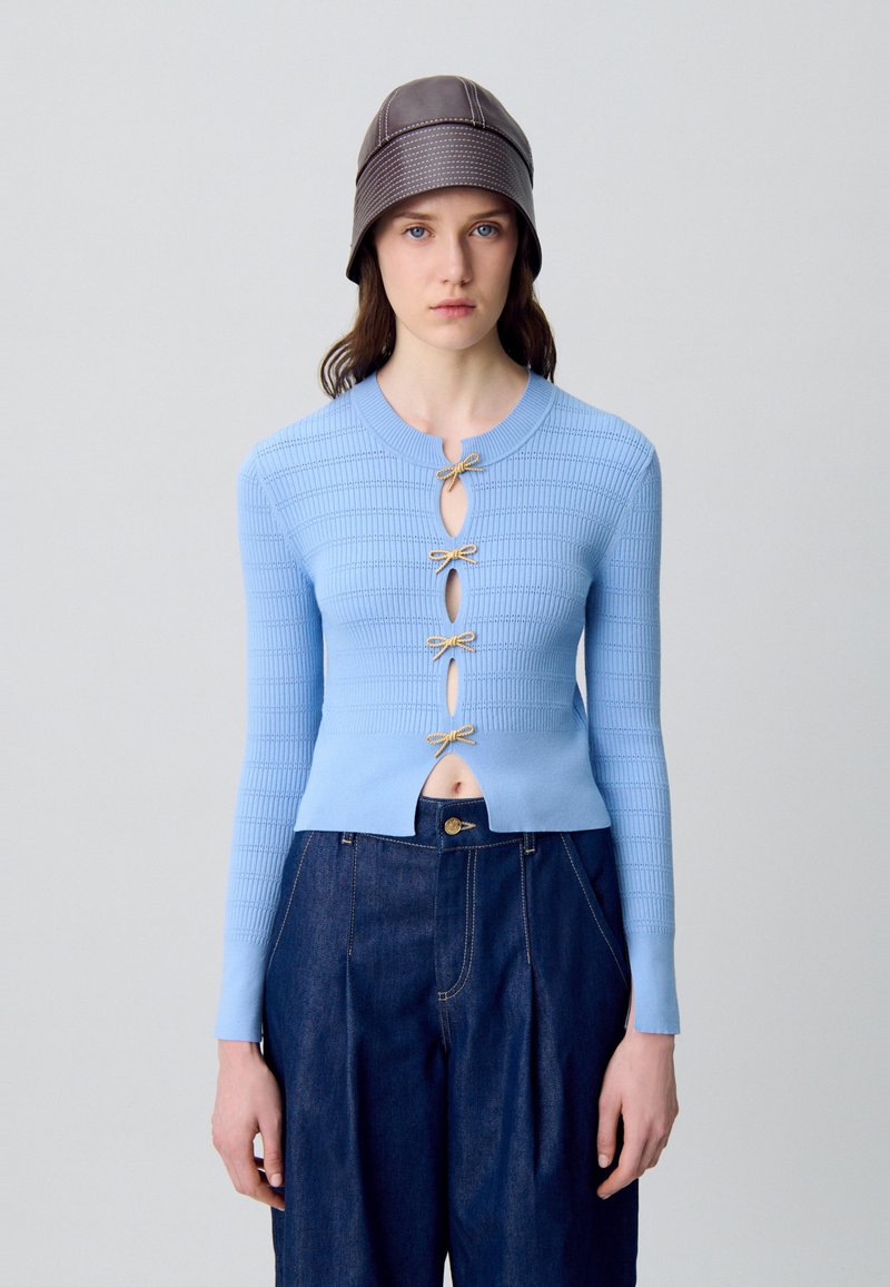 Top a coste di colore azzurro chiaro con scollatura rotonda, decorato con cinque fiocchi d'oro nella parte anteriore e un design corto, abbinato a pantaloni di jeans scuri.