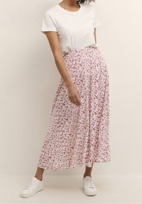 Jupe longue et fluide avec un fond blanc, ornée d'un imprimé floral rose et vert. Associée à un t-shirt blanc uni et des baskets blanches.