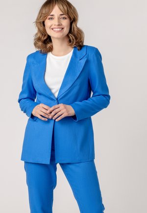 Blue blazer and matching trousers made of textured fabric. Blazer features a notch lapel and two side pockets. White shirt underneath.