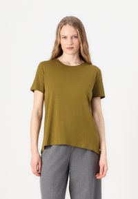 Olivgrön t-shirt med kort ärm och rundad hals, tillverkad av mjuk tyg, och med en förlängd baksöm. Matchad med grå byxor.
