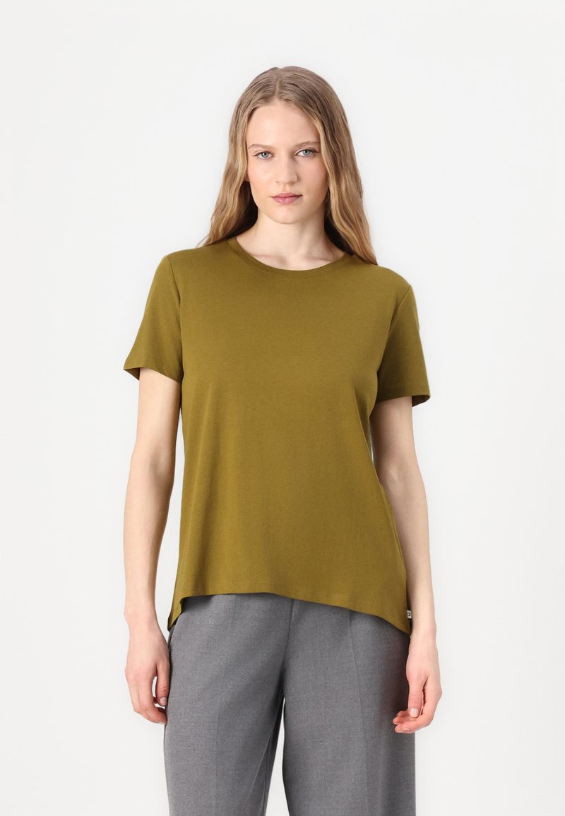 Olivgrön t-shirt med kort ärm och rundad hals, tillverkad av mjuk tyg, och med en förlängd baksöm. Matchad med grå byxor.