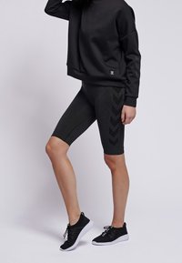 Svart sweatshirt med avslappnad passform och sidologotyp, parat med grå cykelbyxor med ett chevronmönster. Svarta sneakers fulländar looken.