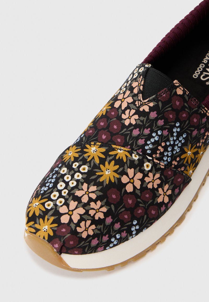 Kwiatowe buty wsuwane z czarną tkaniną na górze i wielokolorowymi wzorami kwiatowymi, elastycznym otworem oraz gumową podeszwą z teksturowanym gripem.