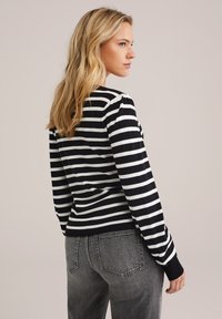 Pull à rayures noires et blanches à manches longues avec un ourlet et des poignets côtelés, associé à un jean gris taille haute.