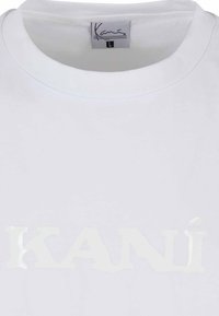 White cotton t-shirt with a round neckline and large glossy "KANÍ" text printed in a slightly raised white font across the front.