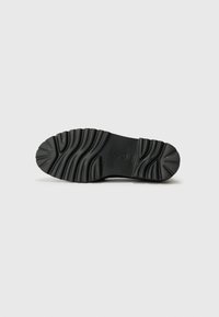 Black rubber shoe sole with a textured, patterned surface. Features grooves for traction and a rounded toe design.