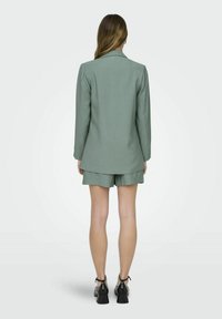 Lichtgroene blazer en shorts set, gemaakt van een gladde stof. De blazer heeft een notch-kraag en een getailleerde pasvorm, de shorts hebben een ontspannen snit.