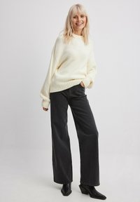 Suéter de punto grueso con cuello y puños acanalados, combinado con vaqueros de talle alto de pierna ancha negros y botines negros de punta.