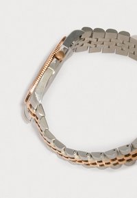 Hihnalla hopea- ja ruusukultaisia kelloja, joissa on uurrettu ruusukultainen kehys ja ruusukultainen kruunu, yksinkertaisella valkoisella taustalla.