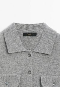 Cardigan gris en maille avec un large col, des boutons noirs devant et deux poches poitrine boutonnées, étiqueté Massimo Dutti.