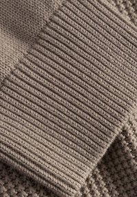 Stickad tyg i en mjuk, dämpad taupe-färg; har ribbat mönster och ett kontrasterande honungscomb-mönster. Slät och varm utseende.