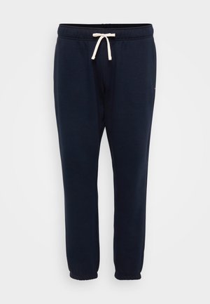 Calças de moletão azul marinho com cintura elástica, cordão ajustável e punhos nos tornozelos. Feitas de um suave tecido de mistura de algodão texturizado.