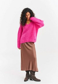 Na dotyk jemný ružový oversized sveter s výstrihom do V, skombinovaný s hnedou saténovou sukňou a hnedými čižmami po kolená s kovovými detailmi.