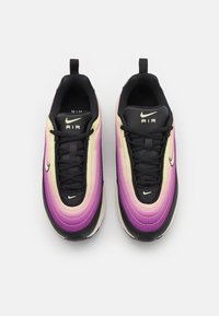 Par de zapatillas Nike Air con un color degradado de púrpura a amarillo, cordones negros y suelas negras vistas desde arriba sobre un fondo blanco.