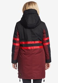 Windbreakerjack met een zwarte bovenkant, bordeauxrode onderkant en rode reflecterende strepen. Inclusief een capuchon en zichtbare ritsdetails.