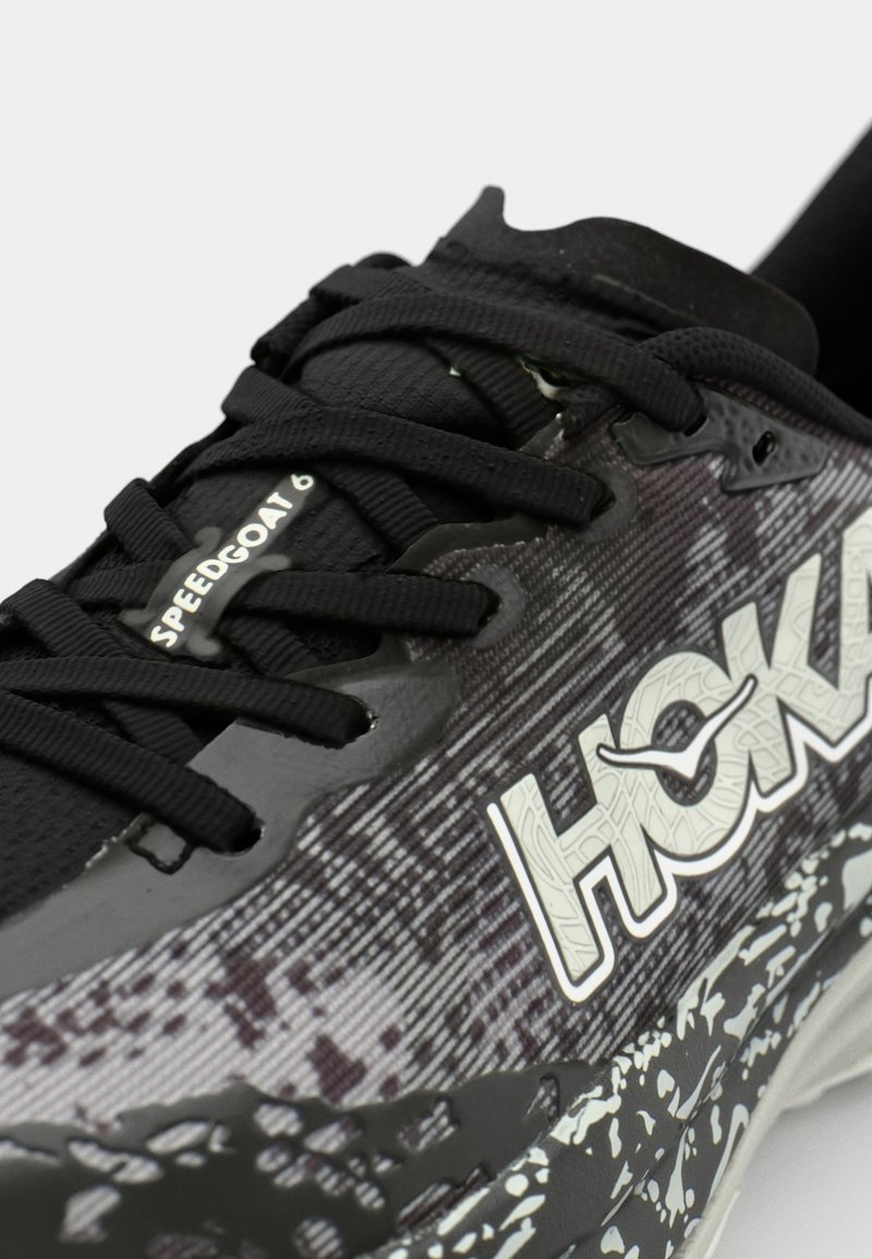 Czarny but do biegania z siateczkową cholewką, teksturowanym gradientowym wzorem, grubą białą podeszwą środkową z czarnymi i szarymi akcentami oraz czarnymi sznurowadłami.