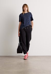 Mørkeblå stripete t-skjorte, løs passform, kombinert med svarte joggebukser, rosa sneakers og en svart totebag. Enkle teksturer, minimalistisk stil.