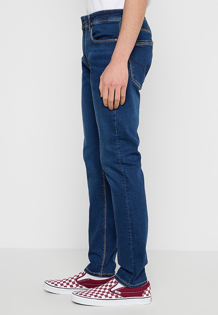 Blaue Denim-Jeans mit geradem Schnitt, klassischer Nähte und Fünf-Taschen-Design, kombiniert mit rot-weißen Karos-Schlüpfschuhen.