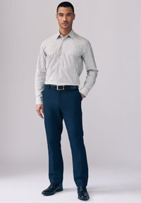 Skjorte med knapper i et lyst mønster med flerfarvede prikker, kombineret med marineblå bukser. Sort bælte og sko fuldender looket.