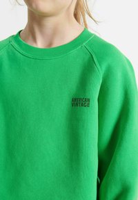 Felpa verde con colletto a coste e maniche raglan. Presenta il logo "AMERICAN VINTAGE" stampato in nero sul petto.