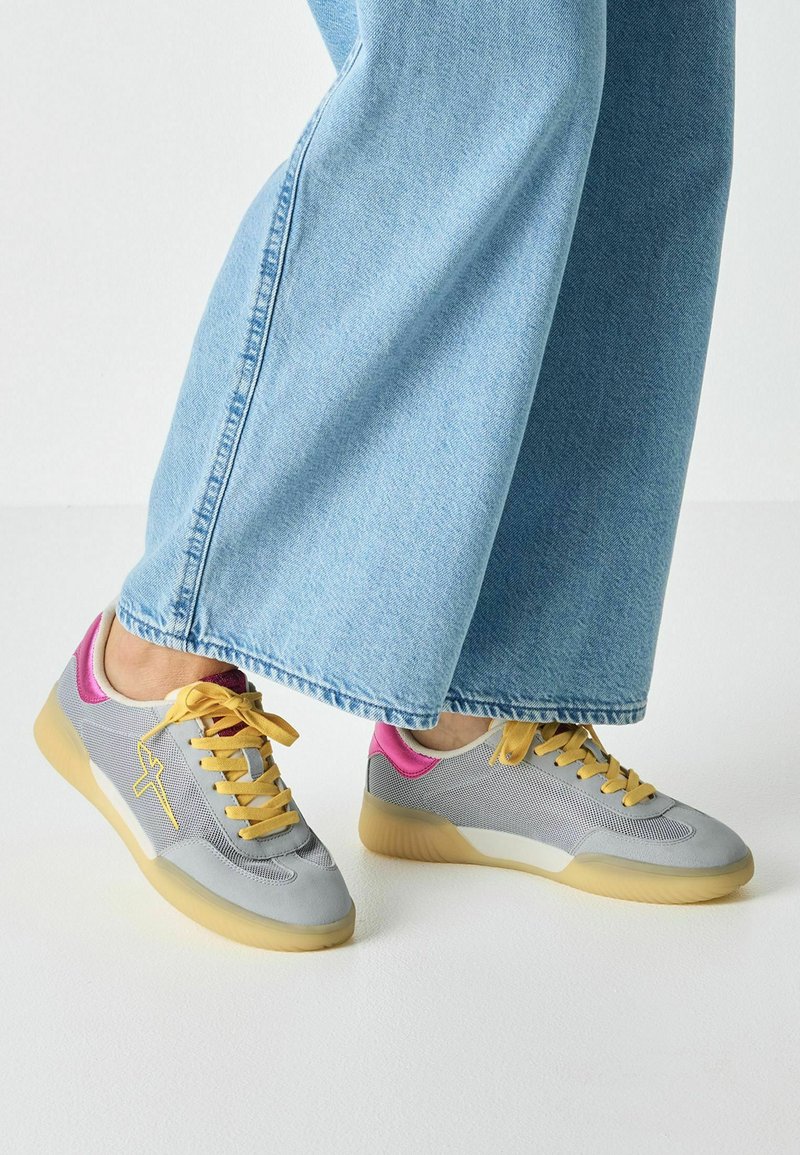 Baskets de sport avec une tige en mesh gris, des lacets jaunes, des accents roses, et une semelle en caoutchouc beige texturée.
