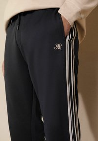 Pantalones deportivos en color navy, hechos de tela suave, con un bolsillo lateral, rayas blancas a lo largo de los lados y un pequeño logotipo bordado en la parte frontal.