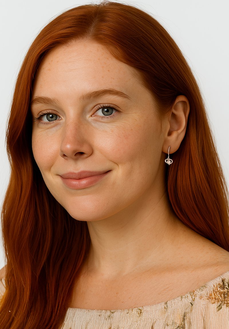 Silverfärgade hängande örhängen med en subtil hjärtformad design som hänger under örsnibben, ihop med en ljus, texturerad top.