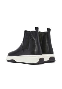 Black leather ankle boots with elastic side panels, a white rubber sole, and a textured back, featuring a sleek design and tab for easy wear.