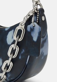 Sac en cuir marine avec un motif marbré, doté d'une chaîne argentée et d'une étiquette. Texture lisse et forme arrondie.