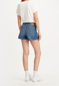 Jeansshorts med hög midja, blå färg, fransad fåll och läderbakpatch. Parat med en vit bomull t-shirt och vita sneakers.