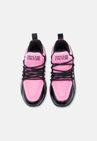 Ροζ και μαύρα αθλητικά παπούτσια Versace Jeans Couture με μαύρα κορδόνια, πλεκτό ύφασμα στην επάνω επιφάνεια και λογότυπο στη γλώσσα, φαίνονται από πάνω.