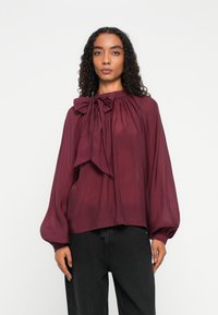 Burgundy blouse with a bow tie at the collar, gathered detail, long balloon sleeves, lightweight fabric, and a relaxed fit.