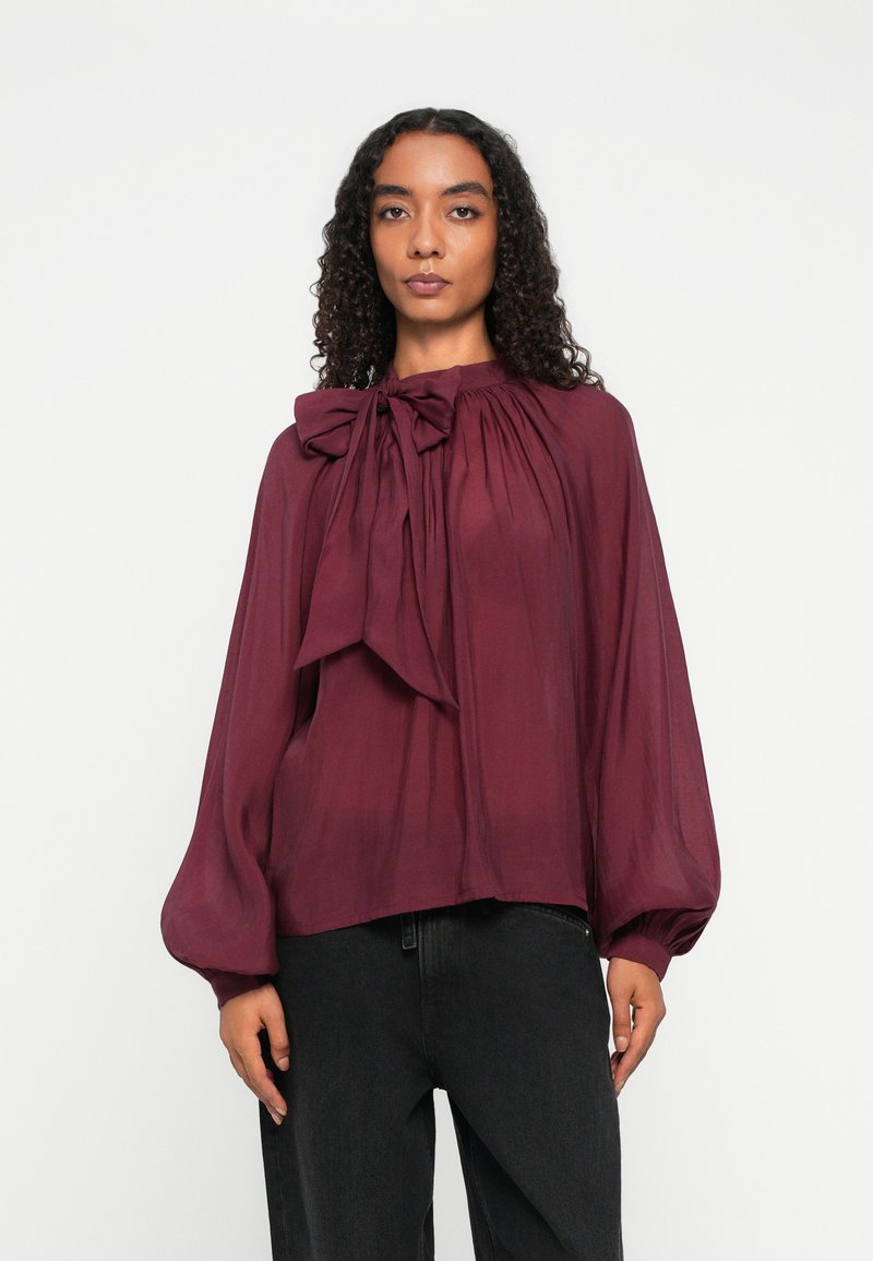 Burgundy blouse with a bow tie at the collar, gathered detail, long balloon sleeves, lightweight fabric, and a relaxed fit.