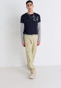 Chemise à rayures marines à manches longues avec le logo "24", associée à un pantalon beige clair et des chaussures crème, présentant une coupe décontractée et une texture douce.