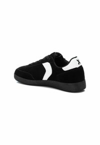 Zapatillas de ante negro con un acento lateral blanco y detalle en el talón. Diseño clásico de tipo bajo con suela de goma negra.