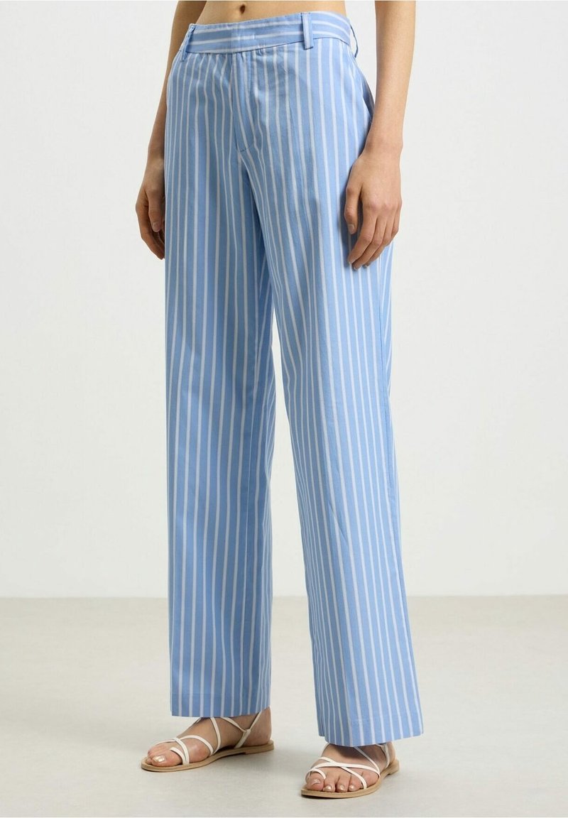 Pantalon large à rayures verticales bleues et blanches porté avec des sandales blanches plates à brides, visible de la taille aux pieds.