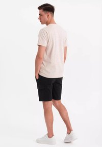 T-shirt beige clair à manches courtes avec des taches multicolores, associé à un short cargo noir et des baskets blanches, vu de dos.