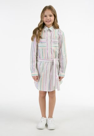Stribet skjortekjole med lange ærmer, knaplukning, to brystlommer, matchende bælte, i pastelfarver på en hvid baggrund. Båret med hvide sneakers.