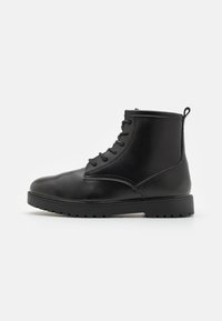 Černá kožená kotníková bota s kulatou špičkou, šněrovacím designem, texturovanou podrážkou a malým poutkem vzadu pro snadné obouvání.