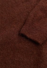 Tissu en maille brun avec une texture douce et duveteuse. Présente un poignet côtelé et un tissage légèrement lâche.