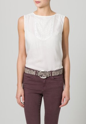 Blouse blanche sans manches avec panneau avant brodé, rentrée dans un pantalon taille haute violet foncé, assortie d'une ceinture en peau de serpent.