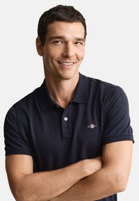 Marineblå polotrøye med korte ermer, to-knapps klaff og logoaccent. Glatt stoff med klassisk passform og en ren halslinje.